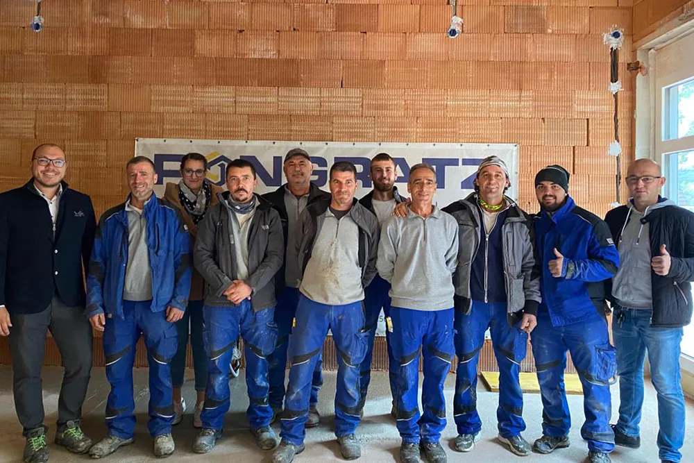 Eine Gruppe von Männern in blauen Arbeitskleidung steht vor einer Wand.